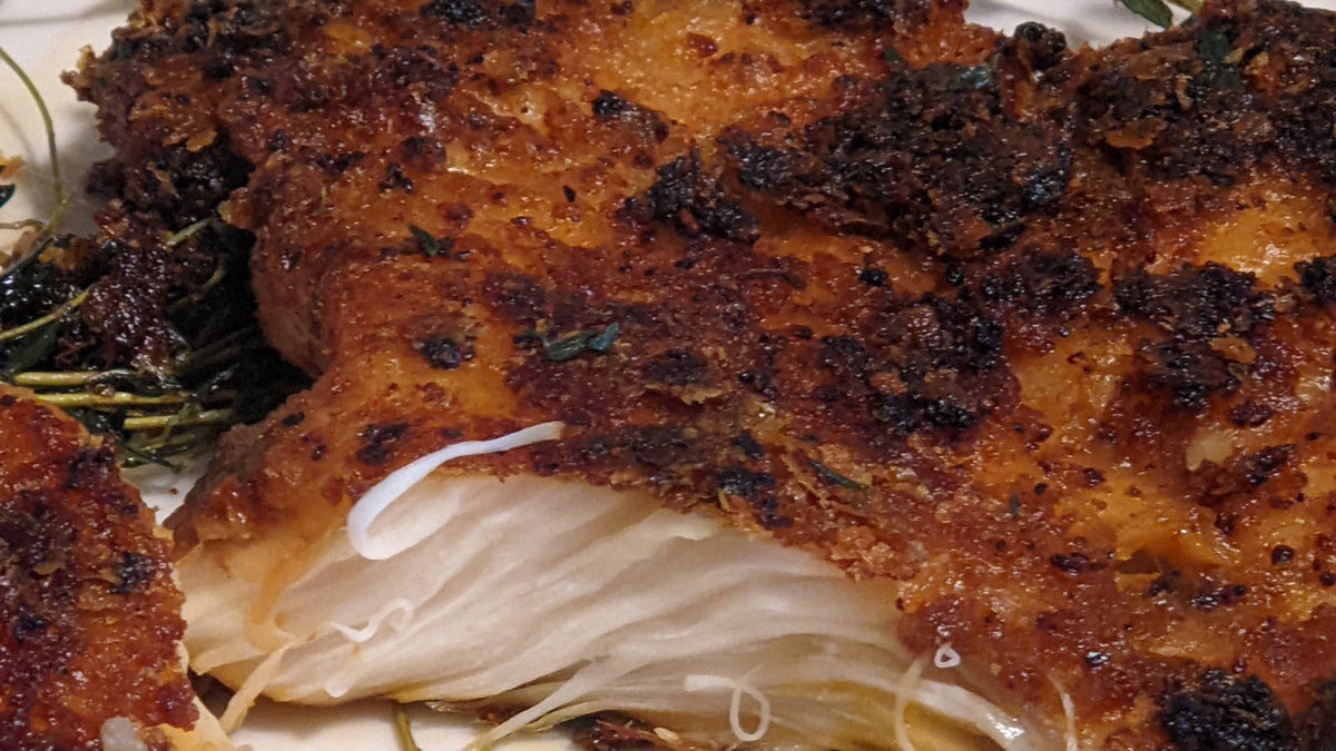 Lion's Mane steaks seared golden brown with thyme on a white plate, one cut open to show the white strands inside